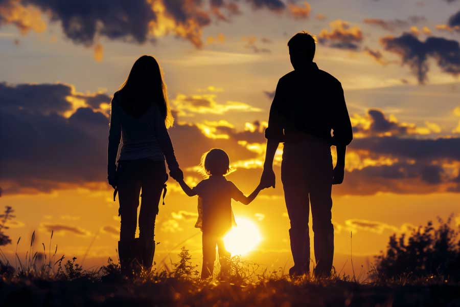 Silhouette of parents each holding a hand of their child facing the sunset