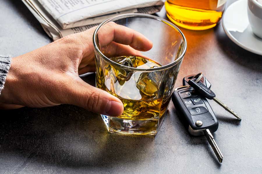 Close on man's hand picking up a glass of liquor next to car keys