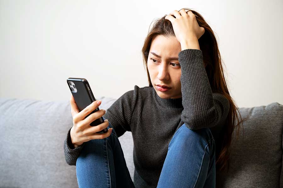 An anxious woman looks at her mobile phone, worrying about bullying on social media.