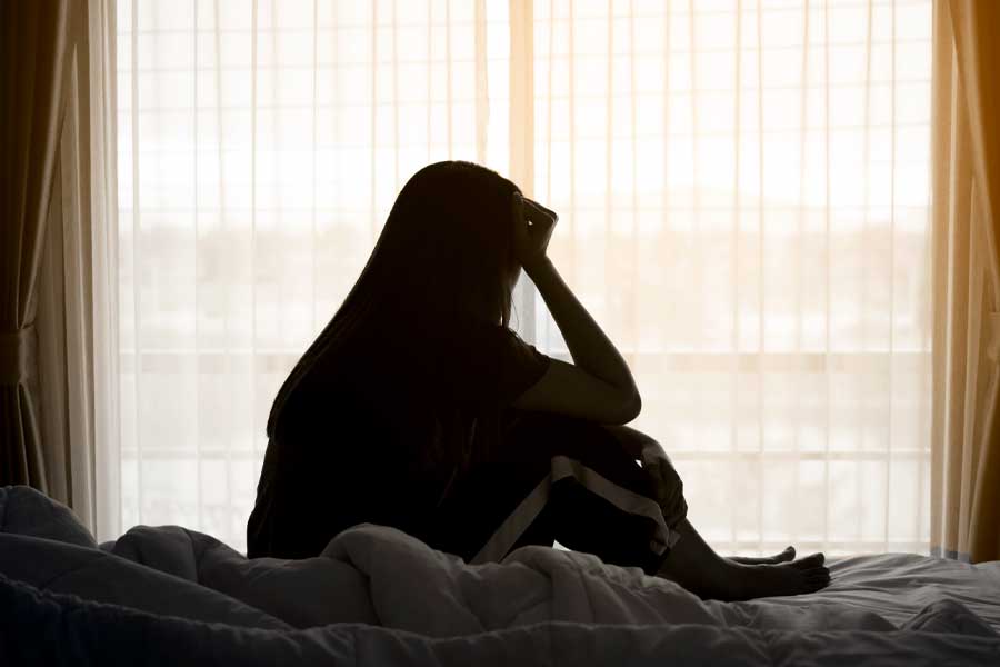 Woman sitting alone on the bed beside the windows.